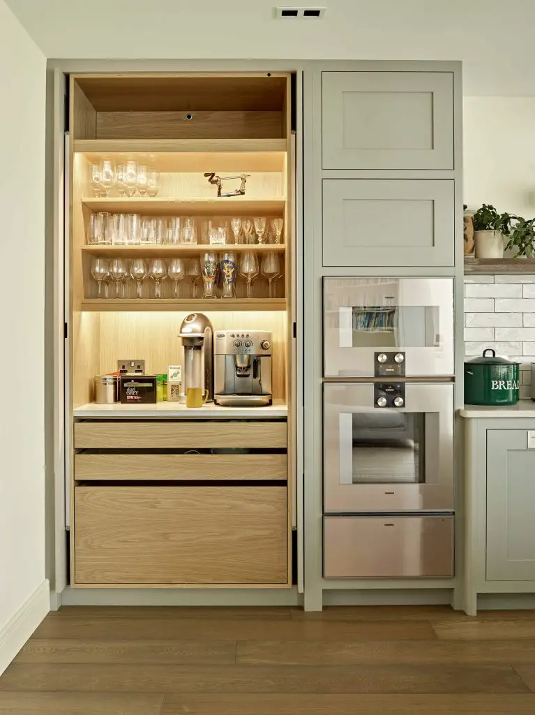 The team at Brayer Design added a custom cabinet with pocket doors that open to reveal a well-lit coffee station. The Shaker-style cabinets in this London kitchen are painted a pale green.