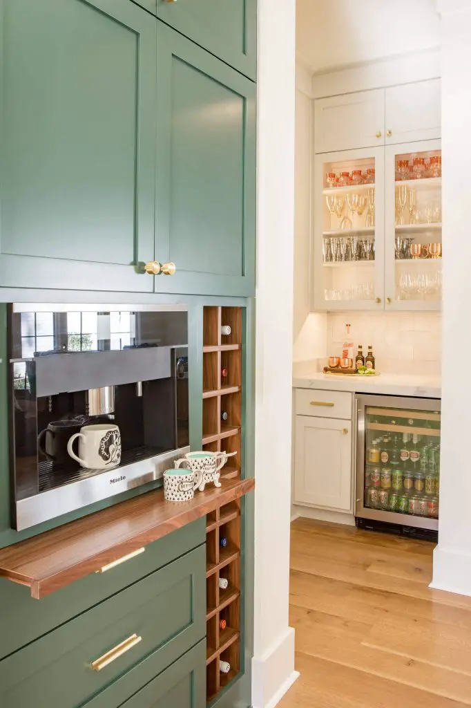 Green cabinets with brass hardware make for a trendy look in this Memphis, Tennessee, kitchen by Lindsey Black Interiors. Note the wood pullout shelf directly below the built-in coffee maker.