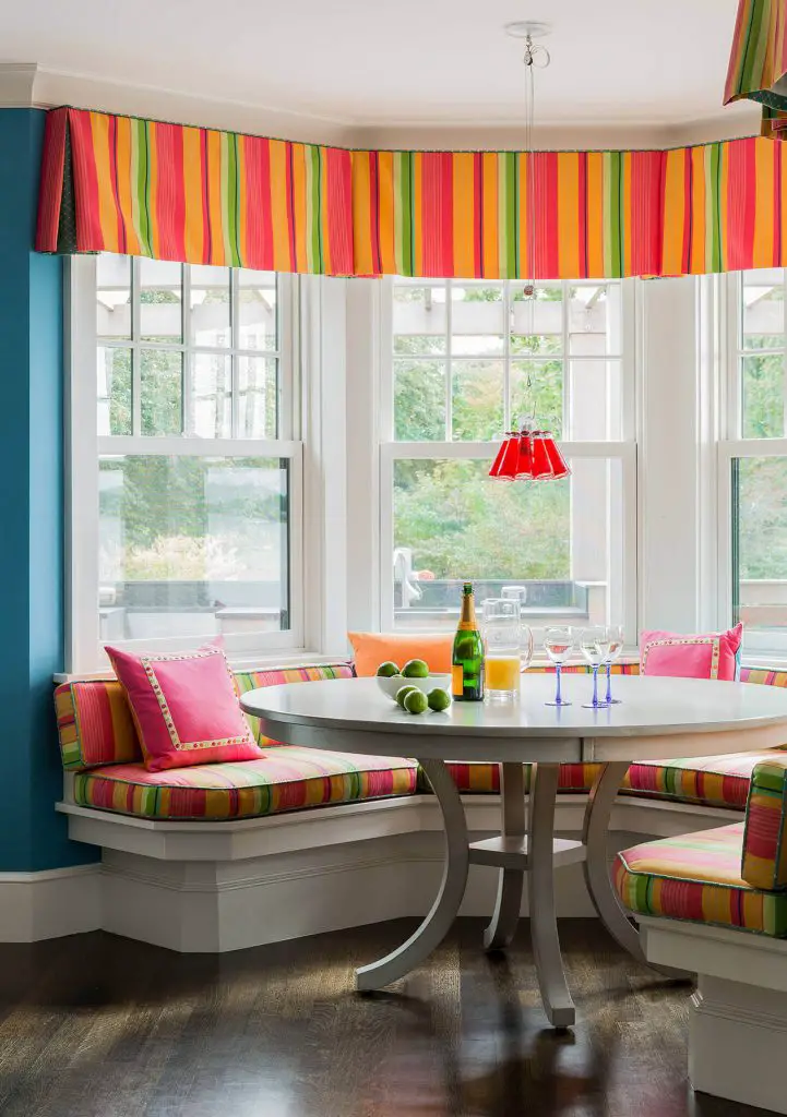 The brightly colored striped fabric that covers the banquette and valance in this Boston kitchen is paired with an Ingo Maurer Campari pendant light