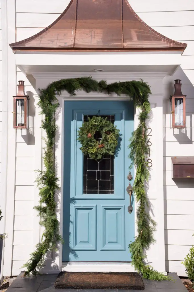 A green swag and a wreath play off this icy blue door beautifully, while copper on the lights, mailbox and pediment are warm touches.